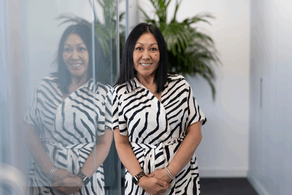 Photo of Bonnie Sartin, Senior Payroll Administrator at GLX who stands against a glass panel, looking at the camera wearing a zebra print dress.
