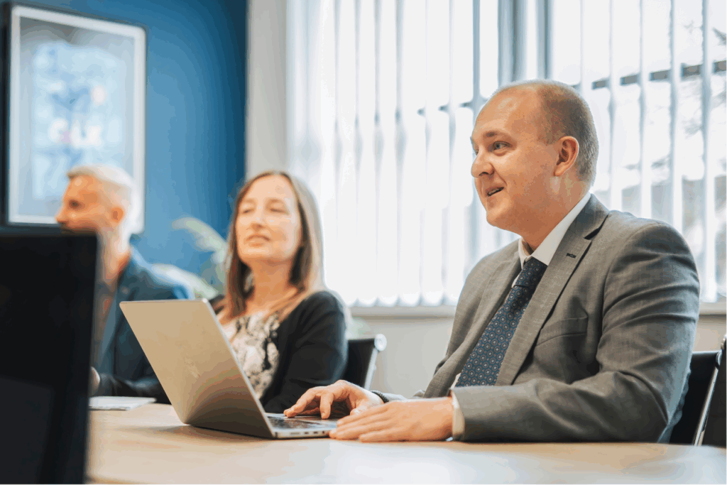 Steven Hemp from GLX Advisory sits next to Jo Leonard from GLX Accounting at the boardroom table talking to someone off-camera. Glenn Matthews from GLX Advisory can be seen in the blurred background.