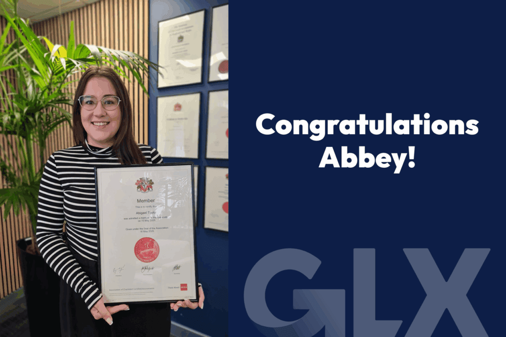Abigael Taylor becomes ACCA qualified and holds up her ACCA certificate in a frame with the words "Congratulations Abbey" while stood in front of the wall of certificates in the GLX office.