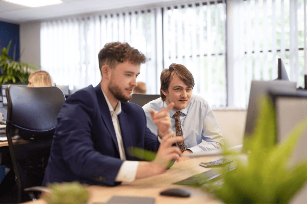 Matt Crabtree sits at his desk pointing to something on his computer screen whilst Charles Two from GLX Advisory looks on.