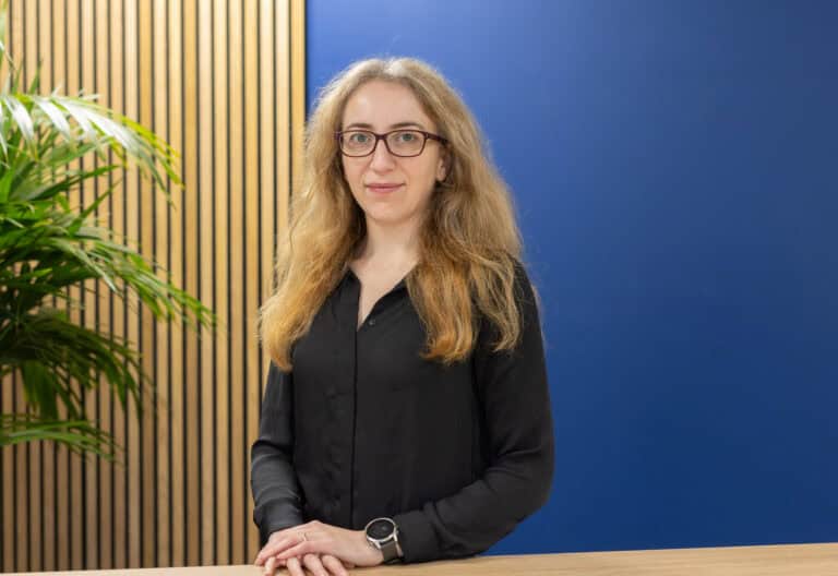 Stephanie Clark from GLX accounting Stands in front of a blue wall with wood panelling to the left in the background.
