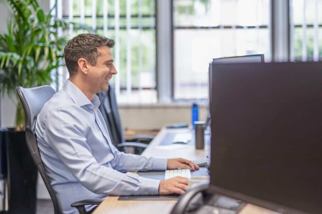 2026 Spring Budget featured image. Side-on view of Graham Dale, Director at GLX, who sits in an office chair facing the right hand side and looking at a screen. Graham wears a blue shirt and his right hand is using the mouse. This image supports the 2026 Spring Statement article