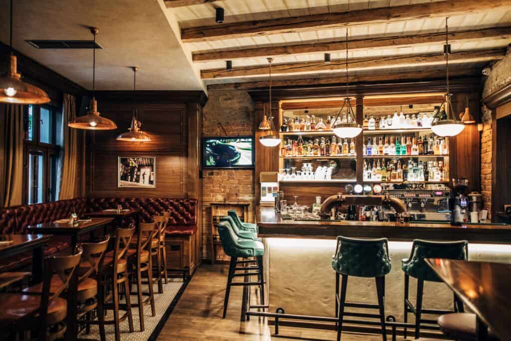 Shot of the interior of a pub with leather sofas and chairs to the left, and a bar to the right with bar stools.